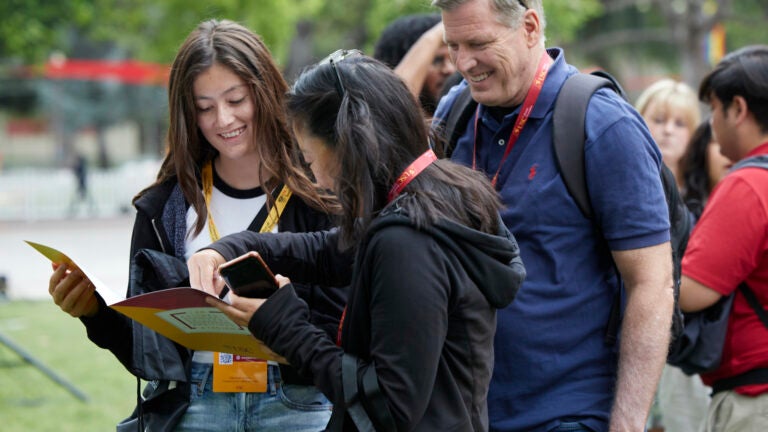 Two parents excitedly looking at USC Orientation flyer with prospective student at Orientation Event.